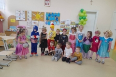 Grupa dzieci stoi w rzędzie w sali przedszkolnej, większość z nich jest przebrana za postacie bajkowe, 4 chłopców siedzi na podłodze. W tle widać kolorowe gazetki.