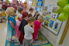 Grupa dzieci stoi przed tablica, oglądają ilustracje do bajek, odgadują tytuły