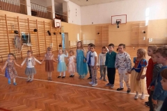 Duża grupa dzieci stoi tworząc się za ręce tworząc półkole.  W tle  widać  drabinki gimnastczne.