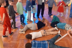 pięcioro dzieci lezy na podłodze. Pozostałe dzieci trzymają się za ręce tworząc półkole.