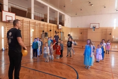 Dzieci stoją w trzech rzędach. Przed nimi pan w ciemnym stroju.