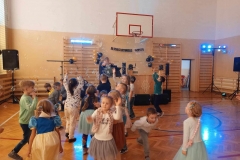 Grupa dzieci znajduje się w sali gimnastycznej. Wszystkie dzieci są w pozycji stojącej.