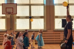 Grupa dzieci stoi w rozsypce. Przed nimi stoi osoba dorosła.