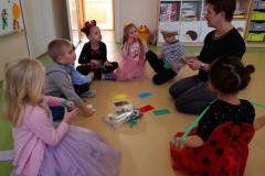 Dzieci siedzą w kole z wychowawcą, na podłodze leżą kolorowe karteczki, dzieci wróżą z kolorów.