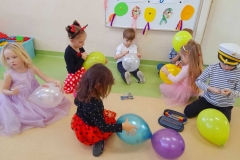 Kilkoro dzieci siedzi pod tablicą, rysują po kolorowych balonach.