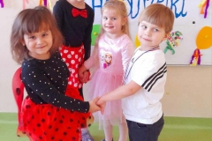 Trzy dziewczynki I chłopczyk tańczą w kółeczku do muzyki. W tle tablica z napisem andrzejki.