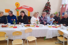 Babcie, dziadziowie i goście siedzą wokół stołu.