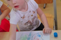 Dziewczynka siedzi przy stoliku, sięga po sól, przed nią ilustracja kolorowego motyla.
