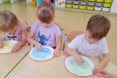 Dwie dziewczynki I chłopiec pocierają sól kolorową kredą.