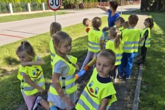 Dzieci ubrane w kamizelki odblaskowe oglądają znaki drogowe podczas spaceru.
