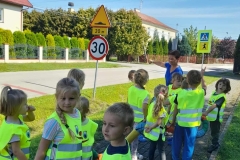Dzieci ubrane w kamizelki odblaskowe oglądają znaki drogowe podczas spaceru.