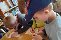 Dziewczynka I chłopiec stoi przy stole, przeglądają książeczki. W dali widać inne dzieci.