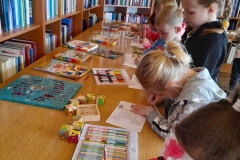 Dzieci stoją wokół stołów, kolorują labirynt  na stołach widać rozłożone książki.