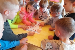 Grupa dzieci stoi wokół stołu, na kartce Nasi czytelnicy odbijają swój palec czerwonym tuszem.