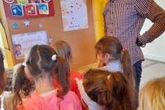 Kilkoro dzieci stoi przed tablicą na której wisi karta pt. Nasi czytelnicy, obok dzieci stoi Pan Paweł