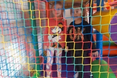 Dwie dziewczynki stoją w kolorowym dmuchanym zamku, przed nimi kolorowa siatka.