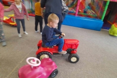 Chłopiec siedzi w czerwonym autku, porusza się nim po dywanie. Przed nim stoi inne autko w kolorze różowym.