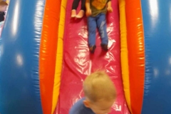 Dwóch chłopców i dziewczynka zjeżdżają z kolorowej dmuchanej zjeżdżalni.