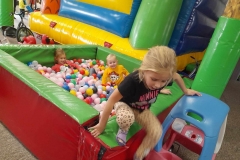 Dziewczynka I chłopiec bawią się w dmuchańcu z kolorowymi piłeczkami, druga dziewczynka wychodzi z dmuchańca.