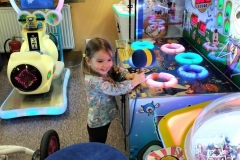 Dziewczynka stoi wśród kolorowych urządzeń.  Są to kolorowe kółka,  niebieska pufa