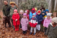 Dzieci stoją przed paśnikiem wraz z członkami Koła Łowieckiego.