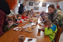 Dzieci siedzą przy stolikach, jedzą kiełbaski i ciasteczka.