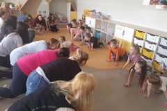 W sali przedszkolnej znajduje sie duża grupa dzieci i rodziców. Znajdują się oni kręgu, w pozycji na czworaka, odtwarzają zaproponowaną im zabawę.