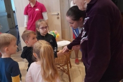 Chłopiec wita się z panią z Domu Pomocy Społecznej, w tle widać inne dzieci i pracowników Domu Pomocy.