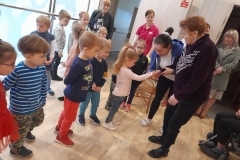 Dziewczynka podaję rękę pani z Domu Pomocy, wokół nich stoją inne dzieci i opiekunka z Domu Pomocy.