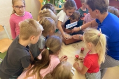 Dzieci siedzą na gazetach, przesuwają się do przodu na sygnał.