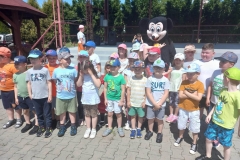 Grupa dzieci w kolorowych strojach stoi w dwuszeregu. Pośrodku stoi myszka.