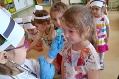 Dziewczynka przebrana za pielęgniarkę bada wzrok drugiej dziewczynce.