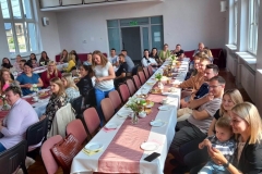 Zdjęcie przedstawia ludzi siedzących przy stole nakrytym białym obrusem.