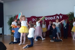 Zdjęcie przedstawia dzieci, które tańczą. Chłopcy kleczą na jednym kolanie, dziewczynki tańczą wokół nich.