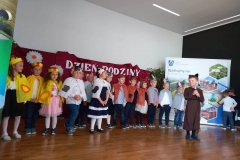 Zdjęcie przedstawia grupę dzieci na scenie. Ubrane w kolorowe stroje.