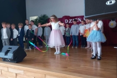 Zdjęcie przedstawia grupę dzieci w kolrowych strojach. Dziewczynka trzyma w rękach kolorowe wstążki.