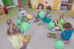 6 dzieci siedzi na podłodze.  Przed nimi leżą obrazki z kwiatkami w kolorze białym.