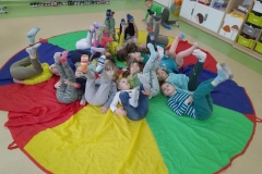 Grupa dzieci leży na kolorowej chuscie animacyjnej, na stopach mają kolorowe, różne skarpetki, naśladują jazdę rowerem