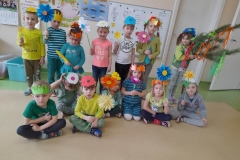 Na zdjęciu grupa dzieci, część z nich siedzi na podłodze, reszta stoi za nimi w rzędzie. Każde z nich ma na głowie opaskę z symbolem wiosny, w reku trzymają kolorowe kwiaty. Jedna dziewczynka trzyma gaik.