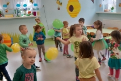 Grupa dzieci stoi w rozsypce na sali, wśród nich są kolorowe balony.