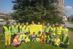 Zdjęcie przedstawia dużą grupę. Część z nich kuca, pozostałe stoją za nimi. Trzymają napis Dzień  Ziemi . W tle widać wysokie zielone drzewo.
