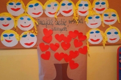 Na tablicy zawieszone uśmiechnięte buzie, plakat: drzewo życzliwości z czerwonych serduszek