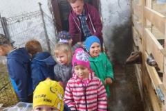 Kilkoro dzieci ubranych w kolorowe stroje stoi w rozsypce na niewielkim korytarzyku w budynku gospodarczym.