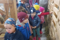 Kilkoro dzieci ubranych w kolorowe stroje stoi w rozsypce na niewielkim korytarzyku w budynku gospodarczym.