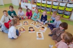 Dzieci siedzą w półkolu, na podłodze rozłożone ilustracje  Dzieci nazywają emocje.