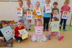 Kilkoro dzieci stoi w rzędzie, przed nimi siedzi czworo dzieci, każde z nich trzyma w ręku bużki  emocje.