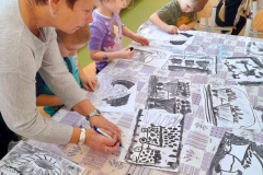 Grupa dzieci siedzi przy stoliku, rysuje węglem, na stoliku leżą pracę dzieci.