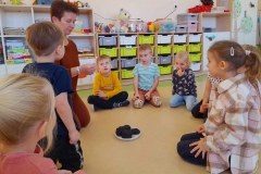 Grupa dzieci siedzi w półkolu, na środku leżą 3 bryły węgla, pani pokazuje zapalona zapałkę.