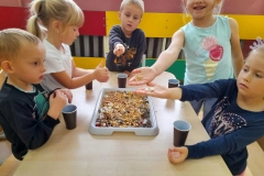 Dzieci siedzą przy stoliku, segregują różne elementy do pojemników