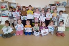 Na zdjęciu widać grupę dzieci ustawioną w dwóch rzędach, w pierwszym rzędzie dzieci siedzą na podłodze, za nimi stoi drugi rząd. Każde dziecko trzyma w rękach swoją pracę.